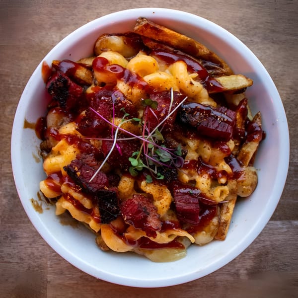 A white bowl of The Flying V's comfort-food mac and cheese with brisket and BBQ sauce.