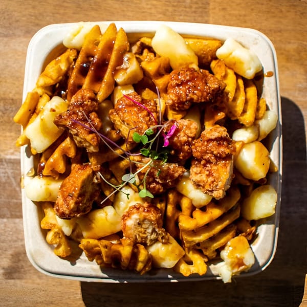 A close-up of The Flying V's poutine with waffle fries, cheese curds, gravy, and crispy chicken.